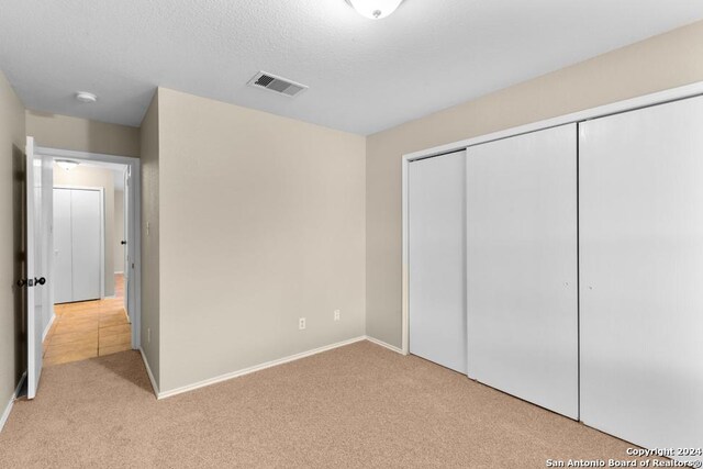 unfurnished bedroom featuring light carpet, a closet, and a textured ceiling