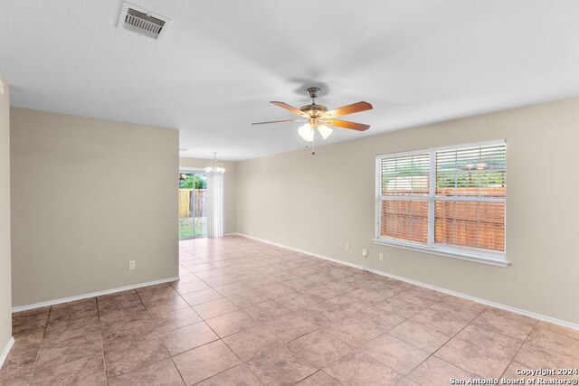 tiled spare room with ceiling fan with notable chandelier