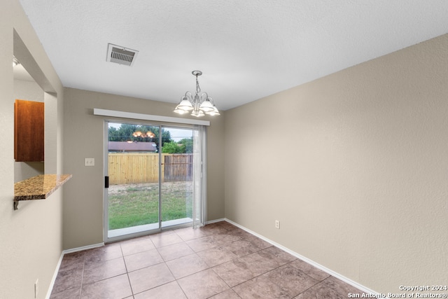 empty room with a notable chandelier, a textured ceiling, and light tile patterned floors