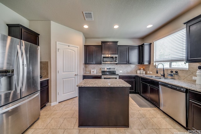 kitchen with appliances with stainless steel finishes, sink, decorative backsplash, a center island, and light stone countertops