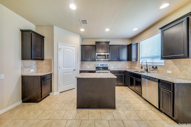 kitchen with sink, stainless steel appliances, dark brown cabinetry, light stone countertops, and a kitchen island