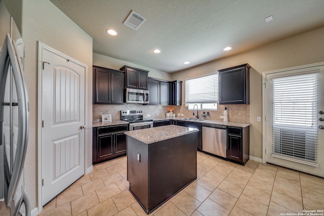 kitchen featuring sink, appliances with stainless steel finishes, a center island, tasteful backsplash, and light stone countertops