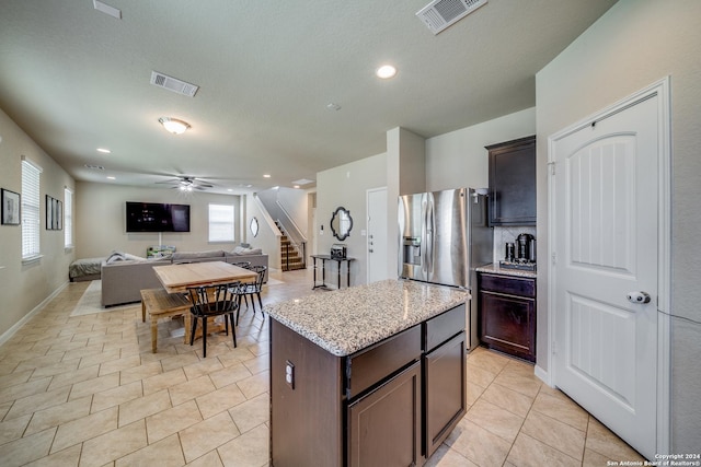 kitchen featuring ceiling fan, light stone countertops, a center island, and dark brown cabinetry