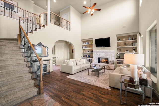 living room with ceiling fan, built in shelves, dark hardwood / wood-style flooring, a high ceiling, and a fireplace