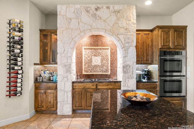 kitchen featuring appliances with stainless steel finishes, decorative backsplash, a textured ceiling, light tile patterned floors, and dark stone countertops