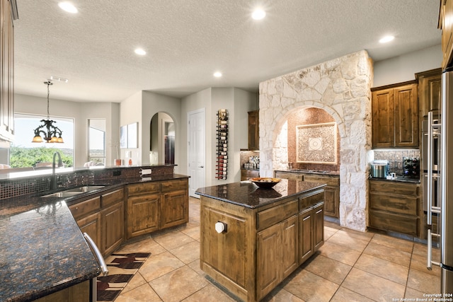 kitchen featuring dark stone counters, a center island, a textured ceiling, light tile patterned floors, and pendant lighting