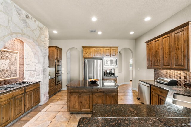 kitchen featuring dark stone counters, backsplash, stainless steel appliances, and a kitchen island