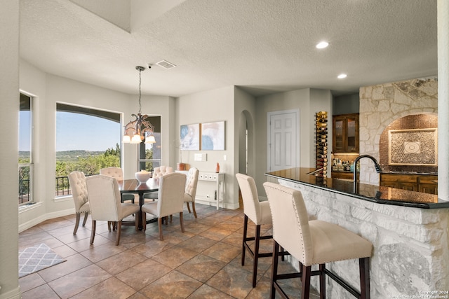 tiled dining room with sink, a notable chandelier, and a textured ceiling