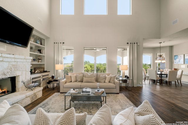 living room featuring a stone fireplace, dark hardwood / wood-style flooring, built in shelves, and a towering ceiling