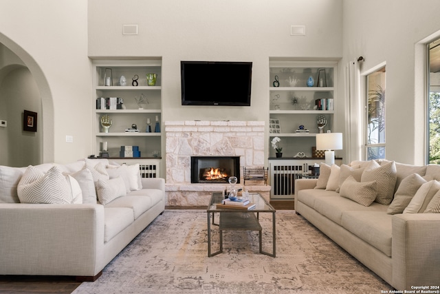 living room with light hardwood / wood-style flooring, a stone fireplace, and built in shelves