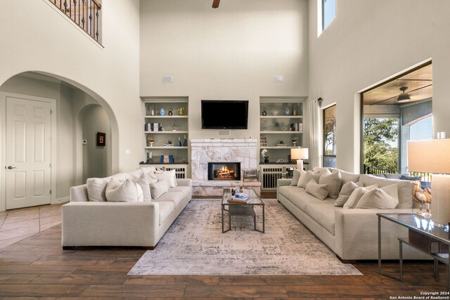 living room featuring built in features, dark wood-type flooring, and a stone fireplace