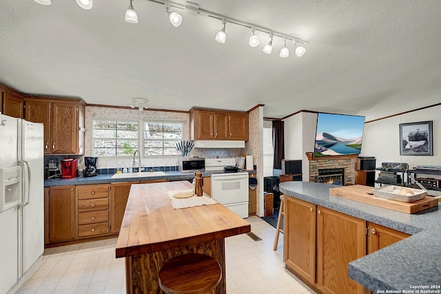 kitchen with wood counters, a fireplace, sink, a center island, and white appliances