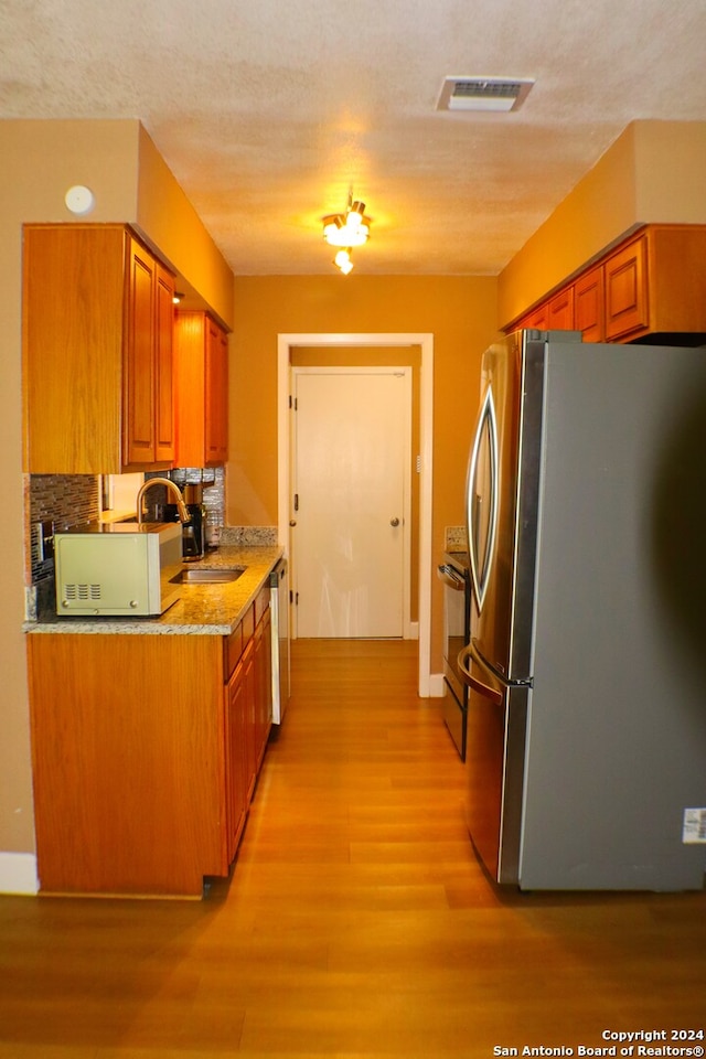 kitchen featuring sink, light stone countertops, appliances with stainless steel finishes, light hardwood / wood-style flooring, and backsplash