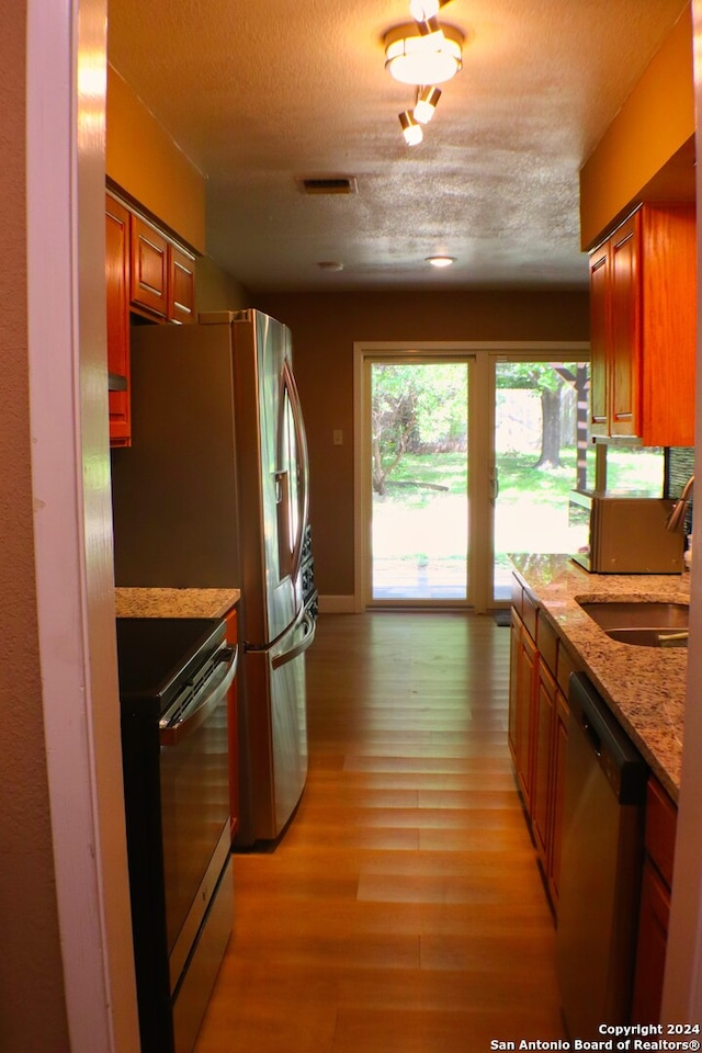 kitchen featuring stainless steel dishwasher, electric stove, sink, light hardwood / wood-style floors, and a textured ceiling