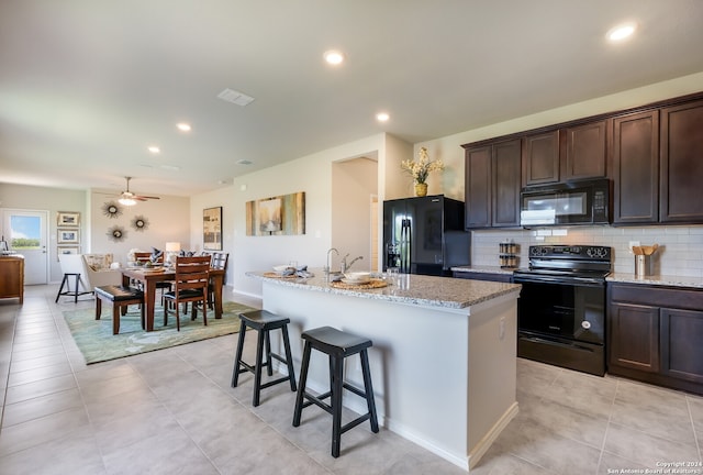 kitchen with light tile patterned flooring, black appliances, light stone countertops, and a kitchen island with sink