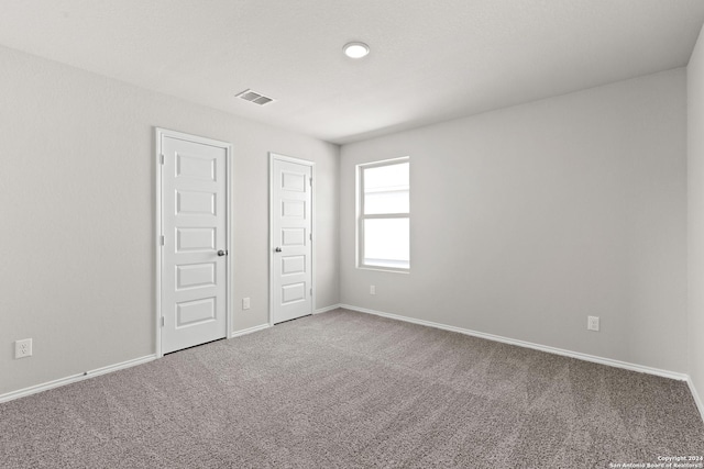 spare room with carpet floors, visible vents, and baseboards