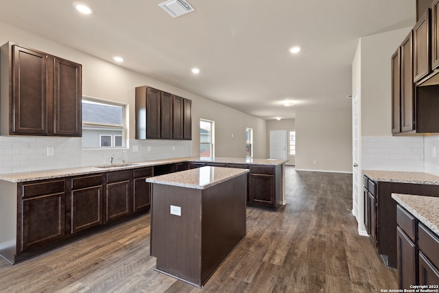 kitchen featuring sink, backsplash, dark brown cabinetry, a kitchen island, and dark wood-type flooring