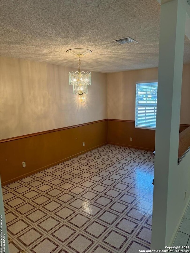 spare room featuring a textured ceiling, light tile patterned floors, and a chandelier