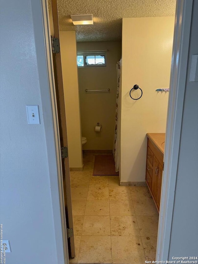 bathroom with a textured ceiling, vanity, tile patterned flooring, and toilet