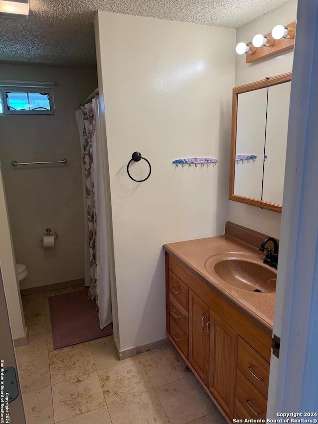 bathroom with a textured ceiling, vanity, tile patterned flooring, and toilet