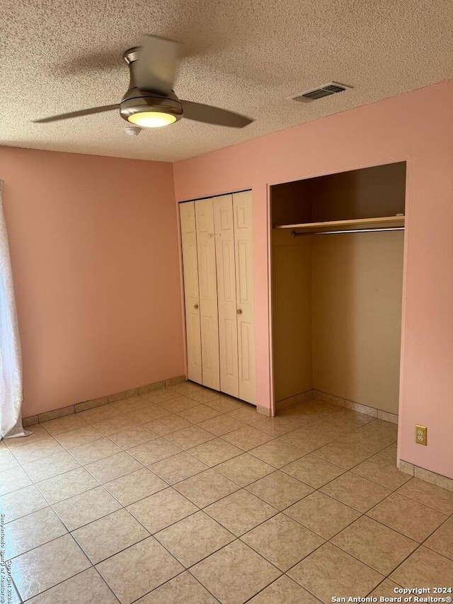 unfurnished bedroom with two closets, ceiling fan, light tile patterned flooring, and a textured ceiling