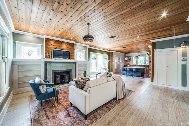 living room featuring ornamental molding, light hardwood / wood-style floors, a brick fireplace, and wooden ceiling