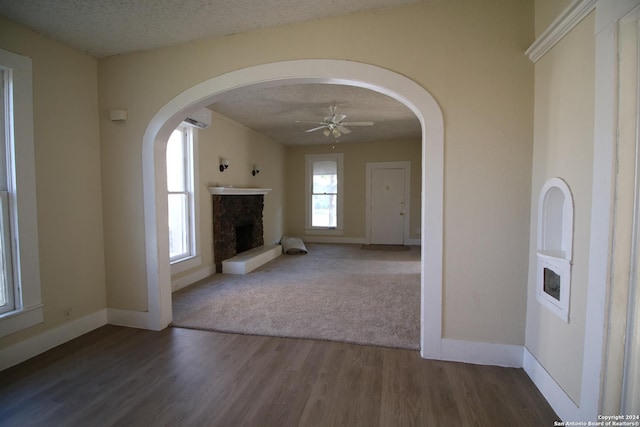 unfurnished living room with baseboards, dark wood finished floors, a stone fireplace, an AC wall unit, and a textured ceiling