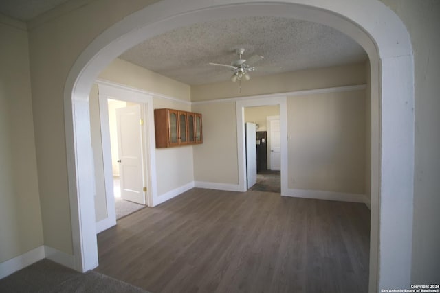 unfurnished room featuring baseboards, arched walkways, a ceiling fan, dark wood-style flooring, and a textured ceiling