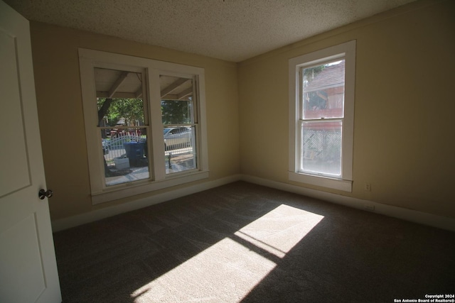 empty room with dark carpet, a textured ceiling, and baseboards