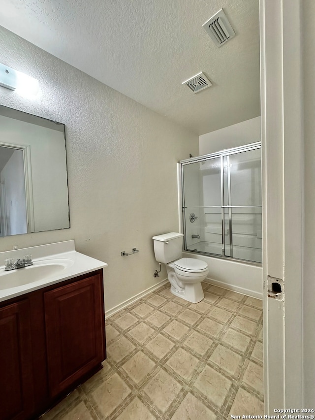 full bathroom with tile patterned flooring, a textured ceiling, toilet, vanity, and combined bath / shower with glass door