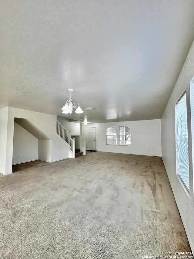 additional living space with plenty of natural light, light carpet, a textured ceiling, and an inviting chandelier