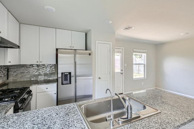 kitchen with tasteful backsplash, sink, white cabinets, stainless steel fridge, and gas stove