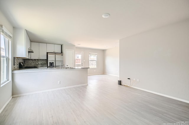 kitchen with tasteful backsplash, white cabinets, kitchen peninsula, stainless steel refrigerator with ice dispenser, and light hardwood / wood-style flooring