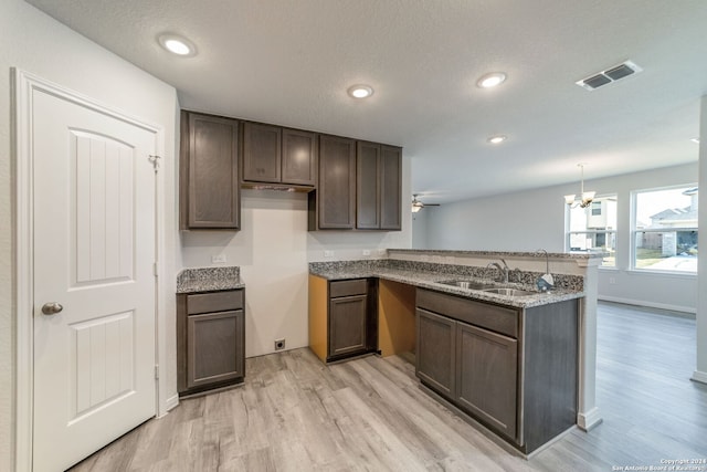 kitchen with kitchen peninsula, ceiling fan with notable chandelier, sink, decorative light fixtures, and light hardwood / wood-style floors