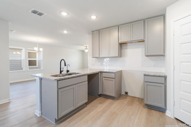 kitchen with gray cabinets, sink, backsplash, light hardwood / wood-style floors, and kitchen peninsula