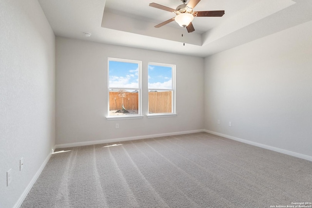 carpeted spare room featuring a raised ceiling and ceiling fan