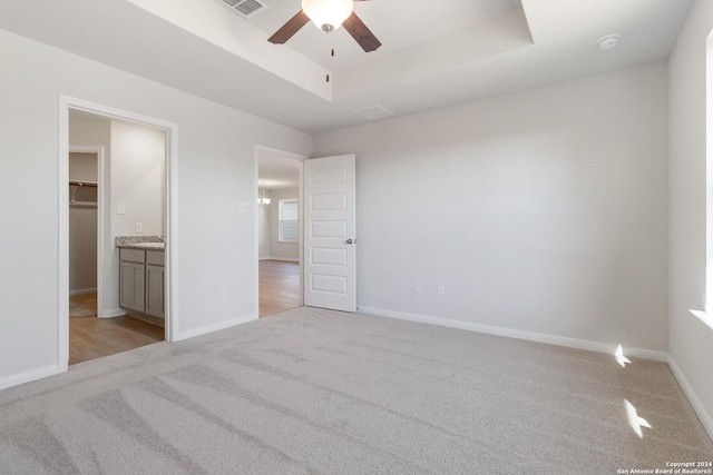 unfurnished bedroom featuring light carpet, a spacious closet, a raised ceiling, and ceiling fan