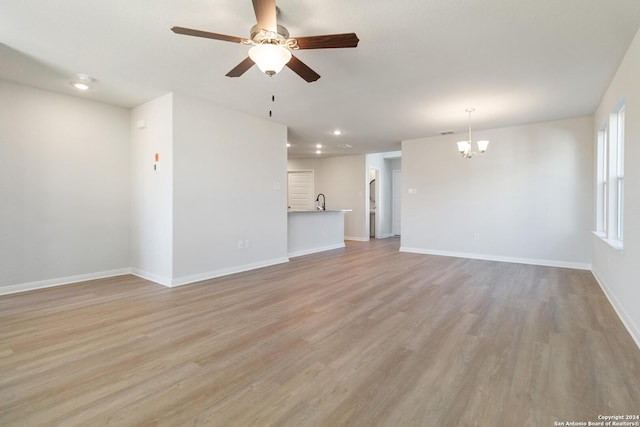 unfurnished living room featuring ceiling fan with notable chandelier and light wood-type flooring