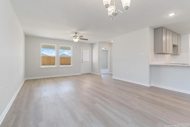 unfurnished living room with ceiling fan with notable chandelier and light wood-type flooring