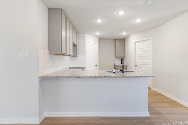 kitchen with sink, gray cabinetry, light stone countertops, kitchen peninsula, and light wood-type flooring