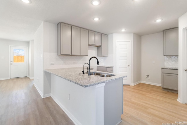 kitchen featuring sink, gray cabinetry, backsplash, kitchen peninsula, and light wood-type flooring