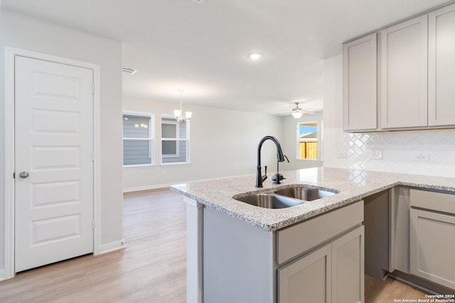 kitchen with sink, gray cabinets, backsplash, decorative light fixtures, and light wood-type flooring