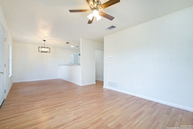 spare room with ceiling fan with notable chandelier and light wood-type flooring