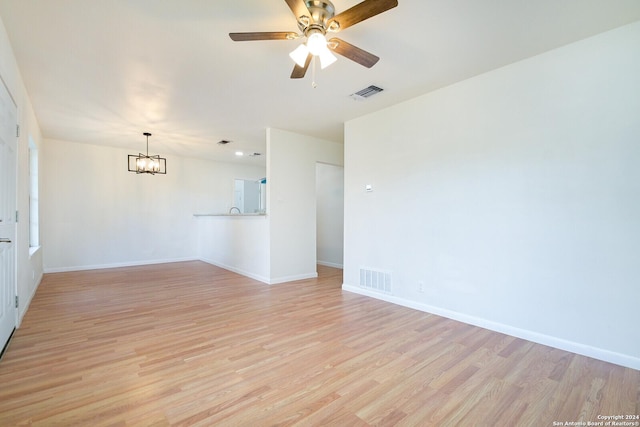 spare room featuring ceiling fan with notable chandelier and light wood-type flooring