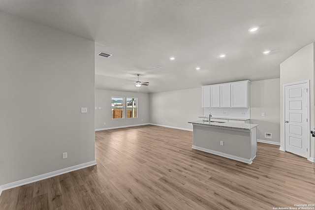 kitchen with white cabinetry, an island with sink, sink, ceiling fan, and light stone countertops