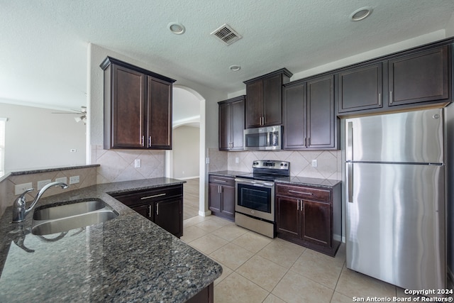 kitchen with dark stone counters, ceiling fan, appliances with stainless steel finishes, decorative backsplash, and sink