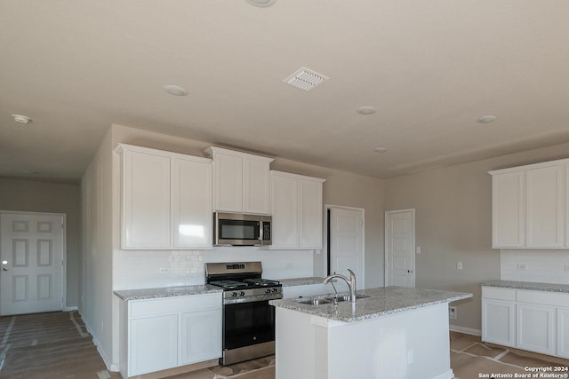 kitchen featuring appliances with stainless steel finishes, an island with sink, sink, white cabinets, and light stone counters