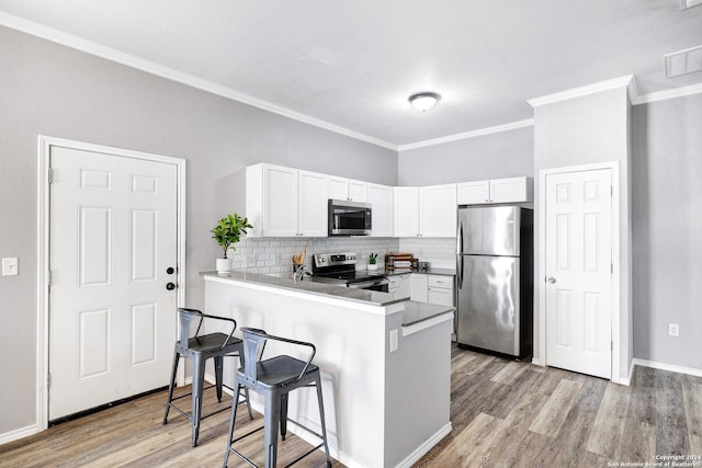 kitchen featuring a breakfast bar area, white cabinetry, kitchen peninsula, stainless steel appliances, and light hardwood / wood-style floors