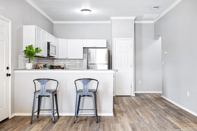 kitchen featuring light wood-type flooring, white cabinets, stainless steel appliances, decorative backsplash, and ornamental molding