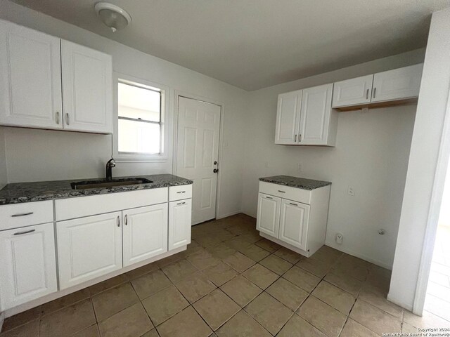 kitchen featuring white cabinets, light tile patterned floors, dark stone countertops, and sink